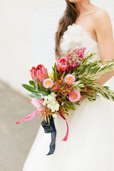 a woman holding a bouquet of flowers in her hand and wearing a white dress with pink accents