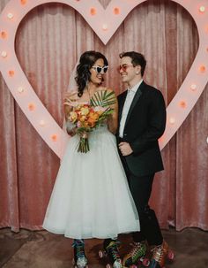 a man and woman standing next to each other in front of a heart shaped sign