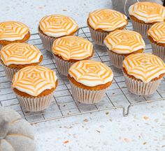 cupcakes with white frosting sitting on a cooling rack next to a pumpkin