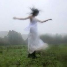 a blurry photo of a woman in a white dress running through a field on a foggy day