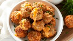 a white bowl filled with meatballs covered in cheese and parsley on top of a wooden cutting board