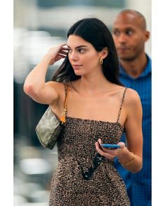 a woman in a leopard print dress is looking at her cell phone while another man looks on