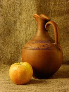 an apple sitting next to a vase on a brown cloth covered table with a tan background