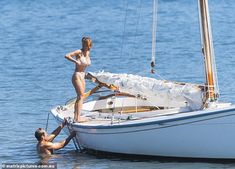 two people on a sailboat in the water with one person helping another to get off