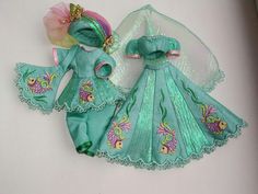 two dolls are dressed up in green and pink outfits, one is wearing a tiara