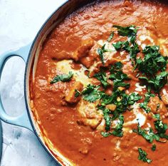 a large pot filled with red sauce and green garnish on top of it