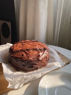 a chocolate frosted cake sitting on top of a white plate next to a window