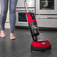 a woman standing next to an oven with a red and black vacuum