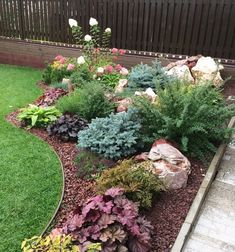 a garden filled with lots of different types of flowers and plants next to a wooden fence