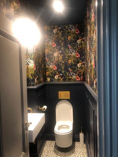 a toilet in a bathroom with floral wallpaper on the walls, and a mirror above it