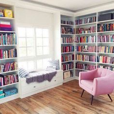 a pink chair sitting in front of a book shelf filled with books