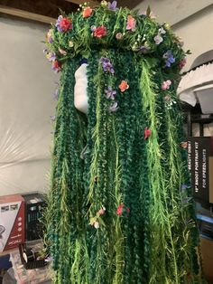 a mannequin made out of grass and flowers on display in a room with other items