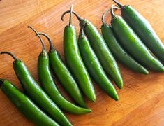 five green peppers sitting on top of a wooden cutting board next to eachother