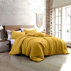 a bed with yellow comforter and pillows in a room next to a brick wall