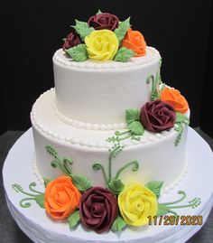 a three tiered white cake with multi colored flowers on it's sides and green leaves