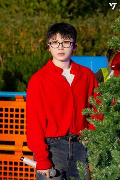 a young boy wearing glasses standing in front of a tree with his hands on his hips