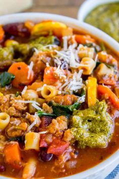 a white bowl filled with pasta and veggies soup next to a green pesto