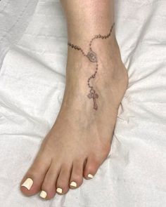 a woman's foot with a rosary and cross tattoo on the side of it