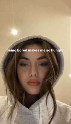 a woman with long hair wearing a hoodie looking at the camera and texting being bored makes me so hungry