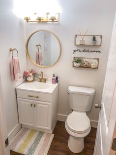 a white toilet sitting next to a bathroom sink under a mirror on top of a wooden floor