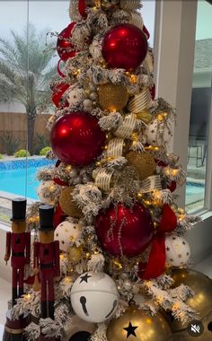 a christmas tree decorated with red and gold ornaments next to a swimming pool in the background