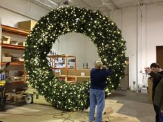 two men working on a large wreath in a warehouse with lights around the wreath,