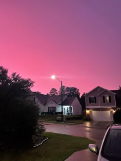 the sun is setting over some houses and cars in front of them on a street