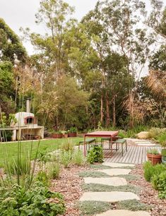 a wooden deck in the middle of a lush green garden with stepping stones leading to a picnic table