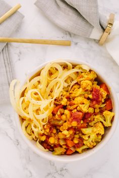 a bowl filled with noodles and vegetables on top of a white tablecloth next to chopsticks