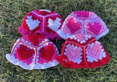 three crocheted hats laying in the grass on top of each other with hearts