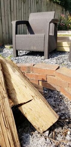 a pile of wood sitting on top of a gravel covered ground next to a chair