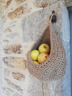 two apples in a woven bag hanging on a stone wall