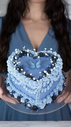 a woman holding a heart shaped cake with blue frosting and white flowers on it