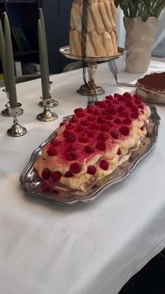 a cake with raspberries on it sitting on top of a table next to candles