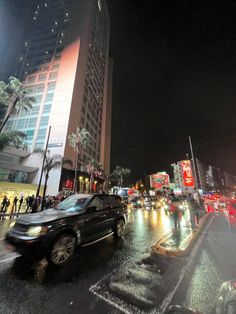 cars are driving down the street at night in front of tall buildings and palm trees