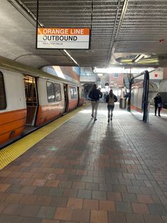 two people are walking towards an orange line train