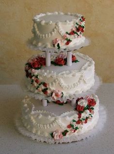 three tiered wedding cake with roses on the top and bottom, sitting on a table