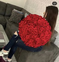 a woman sitting on a couch holding a large bouquet of red roses