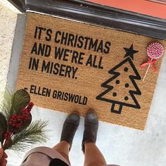 a person standing in front of a christmas door mat that says it's christmas and we're all in misery