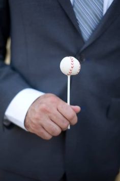 a man in a suit is holding a baseball on a stick with the ball stuck to it