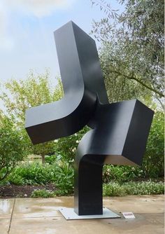 a black sculpture sitting on top of a cement slab in front of trees and bushes