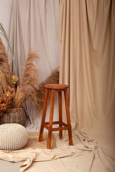 a wooden stool sitting next to a basket filled with dried flowers and plants on top of a rug