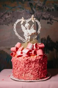 a cake with pink frosting and bows on top is sitting on a table in front of a wall