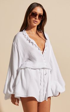 Turn heads in the Laylani Playsuit - V Neck Puff Sleeve In White. This playful and flirty playsuit is perfect for any casual occasion, with its A line shape and white cotton fabric that's both comfortable and chic. The v neck adds a touch of femininity, while the puff sleeves give it a trendy edge. Whether you're dressing up for a night out or keeping it cozy during winter, this long sleeve playsuit will have you looking effortlessly stylish wherever you go. So why wait? Go ahead and add this mu Summer Cotton V-neck Jumpsuit, White Cotton Beach Jumpsuits And Rompers, Summer Cotton V-neck Jumpsuits And Rompers, White Cotton Jumpsuits And Rompers For Beach, Flirty White Top For Vacation, Flirty White Tops For Vacation, White Summer Jumpsuits And Rompers For Loungewear, White Jumpsuits And Rompers For Summer Loungewear, Chic Cotton V-neck Jumpsuits And Rompers