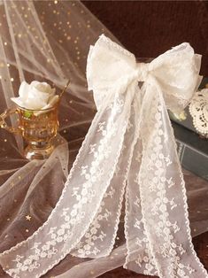 a white lace bow on top of a table next to a glass vase with flowers