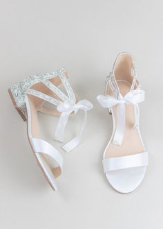 two pairs of white shoes with bows and sequins on the toes, one in satin