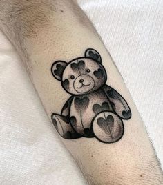 a black and white teddy bear tattoo on the right forearm, with hearts in the middle