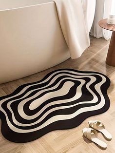 a black and white rug on the floor next to two pairs of slippers in front of a bathtub