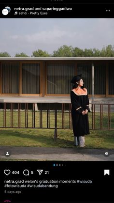 a woman standing in front of a building wearing a black dress and hat with her hands on her hips