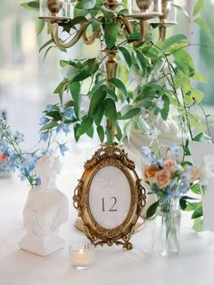 a table topped with a clock surrounded by vases filled with flowers and greenery